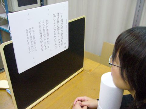 図2.4.5 書見台と顎台を用いて視距離を一定に保っている様子:生徒が発泡スチロールの顎台に顎を載せ、MNREADの読書チャートを一定の視距離を保って読んでいる様子を写した写真